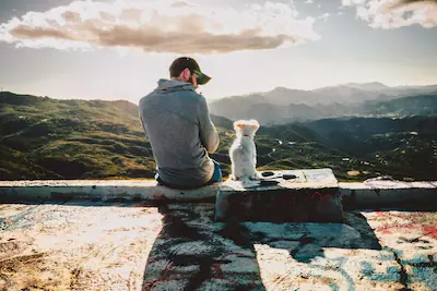 Mann sitzt mit Hund an einem Aussichtspunkt